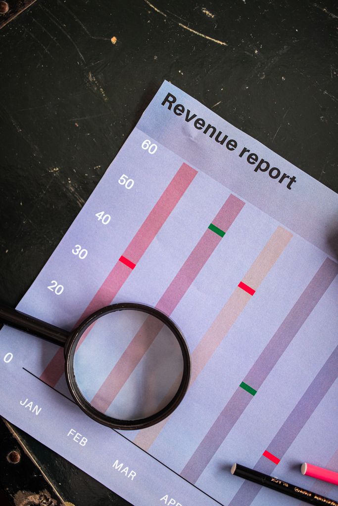 A magnifying glass on a vertical bar chart titled "Revenue report" showing monthly data analysis.